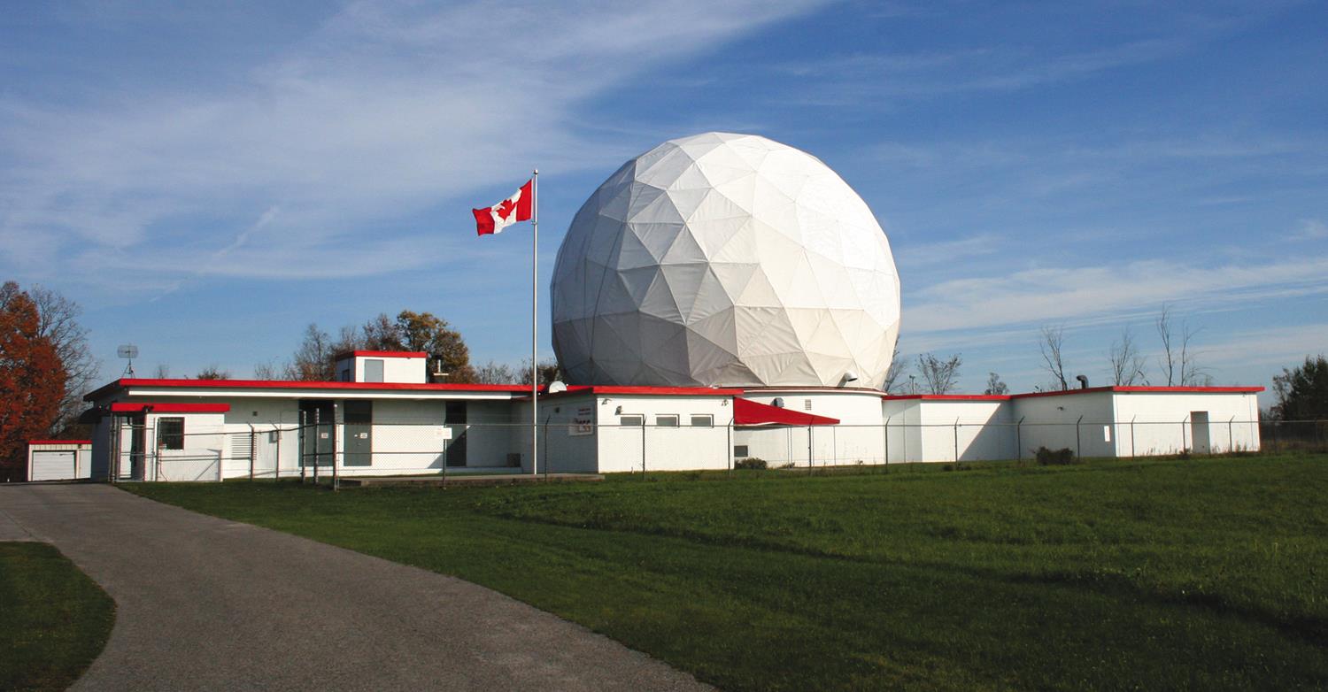 Exterior view of a building with a giant metal space frame radar dome on its roof.